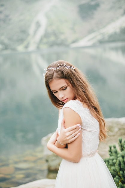 Noiva morena atraente em lindo vestido de noiva branco em pé perto do lago Morskie Oko