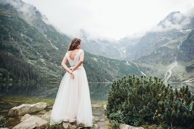 Noiva morena atraente em lindo vestido de noiva branco em pé perto do lago Morskie Oko