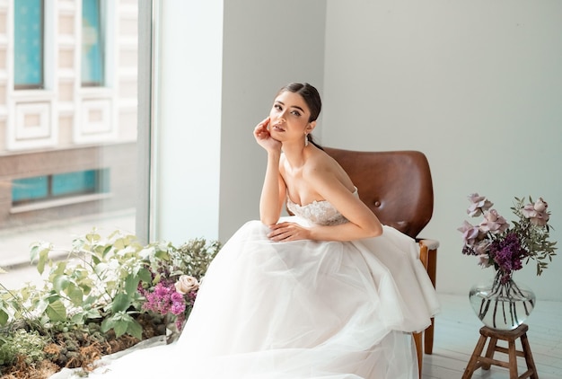 Noiva morena em um vestido branco luxuoso está se preparando para o casamento Preparação matinal A mulher coloca sapatos de casamento