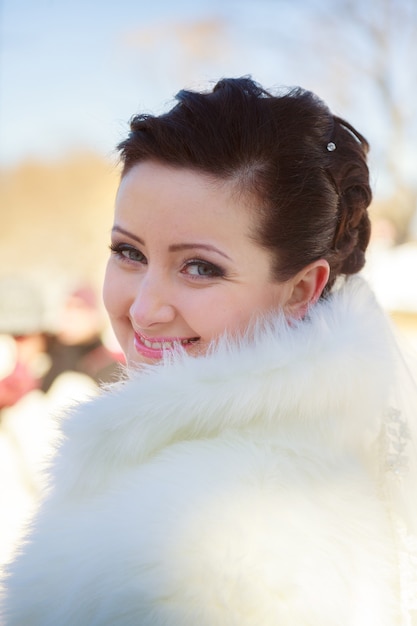 Noiva posando na floresta de inverno com um casaco de pele. Sessão de fotos de casamento em um parque nevado.