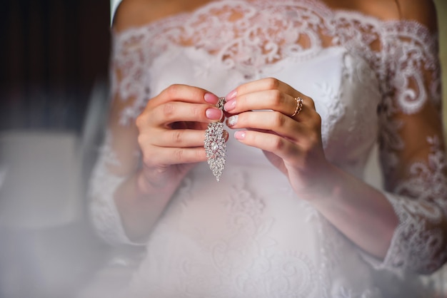 Noiva segurando brincos de noiva em mãos no vestido branco fundo