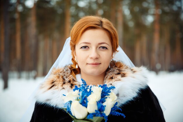 Noiva segurando um buquê de rosas brancas frescas e delfínio com casaco de pele. buquê de casamento criativo de inverno