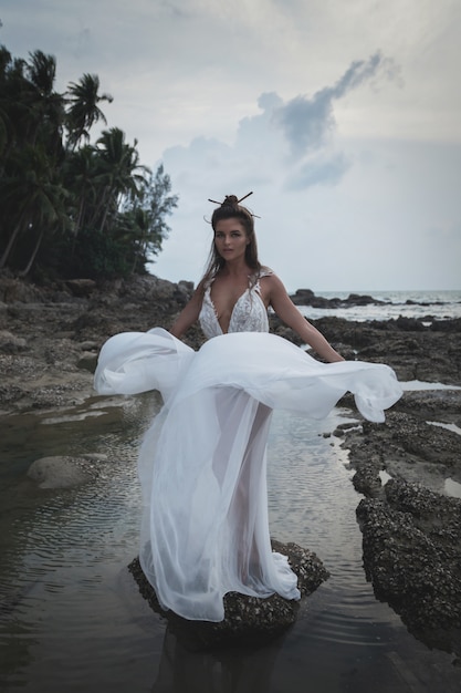 Noiva sensual usando vestido de casamento bonito na praia rochosa
