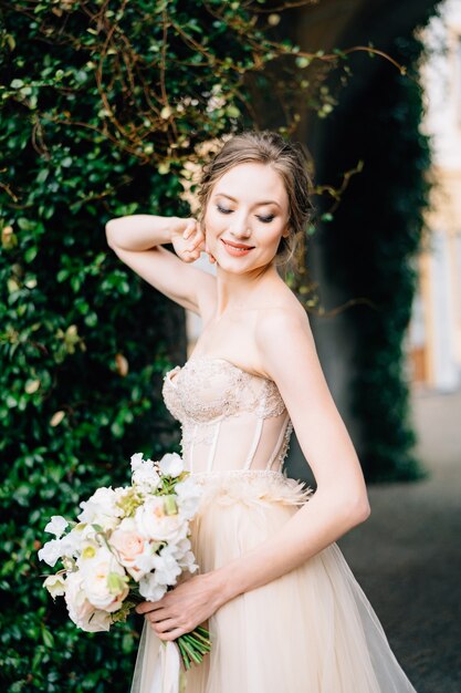 Noiva sorridente em um vestido sem ombro com um buquê de flores rosa colocou a mão atrás da cabeça