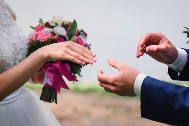 Noivo coloca na mão o anel de casamento de ouro da noiva