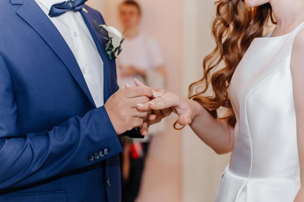 Foto noivo colocando anel de ouro no dedo da noiva durante a cerimônia de casamento mãos com anéis de perto