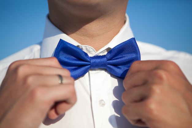 Noivo de camisa branca endireita uma gravata azul contra um céu azul