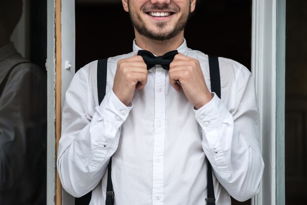 Noivo de camisa branca sorrindo pela janela. em antecipação à noiva.