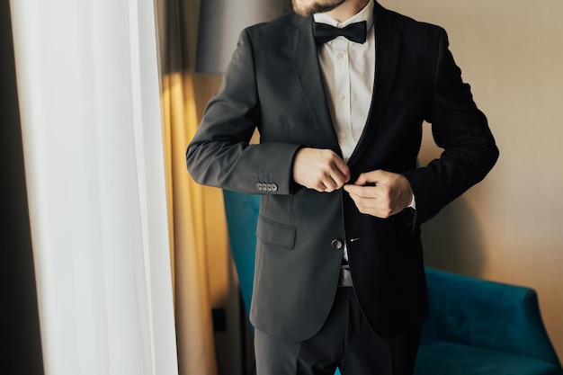 Foto noivo de smoking preto prende nos botões da jaqueta preparativos do casamento no mo