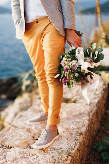 Noivo de tênis com um buquê de flores em pé em um caminho de pedra, close de pernas