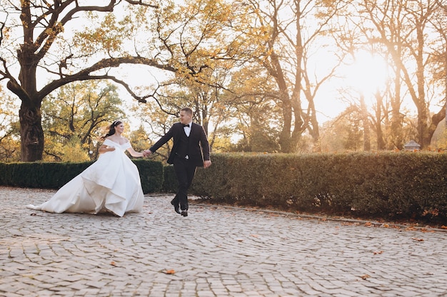 Noivo e noiva felizes correndo alegremente juntos por um caminho no dia do casamento