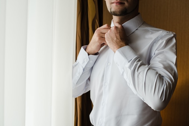 noivo em uma camisa branca um homem abotoa sua camisa as taxas do noivo