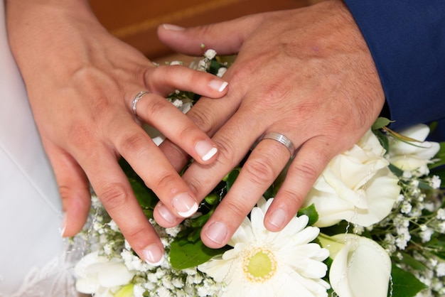 Noivo homem e noiva mulher dedos mãos com alianças de casamento sobre flores de buquê de casamento