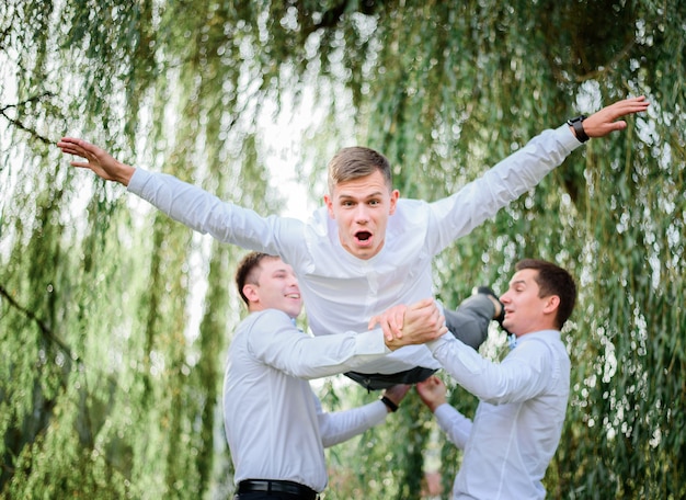 Noivo levanta a mão como um piloto enquanto groomsmen segurá-lo em suas mãos