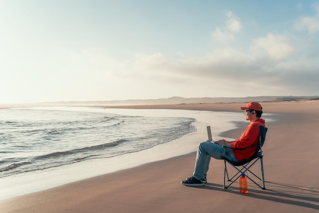 Nômade digital sentado na praia ao ar livre sozinho trabalhando relaxado e olhando para o horizonte