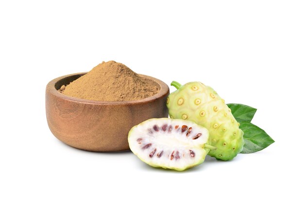 Noni o Morinda Citrifolia en polvo en un tazón de madera con frutas y hojas aisladas sobre fondo blanco.