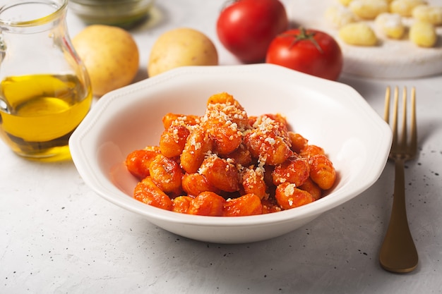 Ñoquis tradicionales con salsa de tomate y queso en un plato blanco con ingredientes sobre una mesa