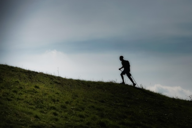 Nordic andando para cima em um prado montanhoso em silhueta