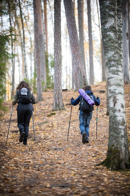 Nordic Walking niño niño y mujer joven en el bosque vista trasera otoño