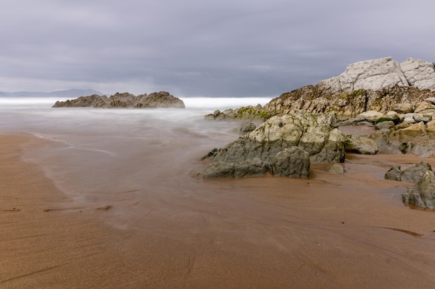 NORDSTRAND MIT WELLEN UND FELSEN UNTER BEWÖLKTEM HIMMEL IM FRÜHLING