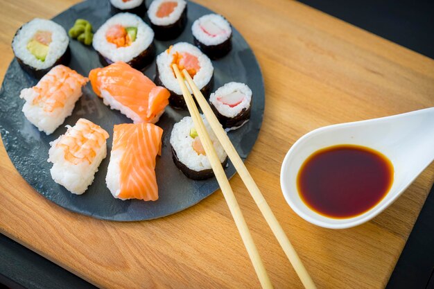 Nori sobre una mesa de madera sobre un plato de pizarra negra con salsa de soja y palillos