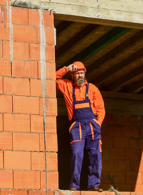 Normaler Tag. Alltag am Bau. Gut erledigt. Mechaniker müde Baumeister entspannend auf der Baustelle. Erbauer, der Zigarette raucht. Pause und entspannen. Bärtiger Mann in Ingenieuruniform und Schutzhelm.