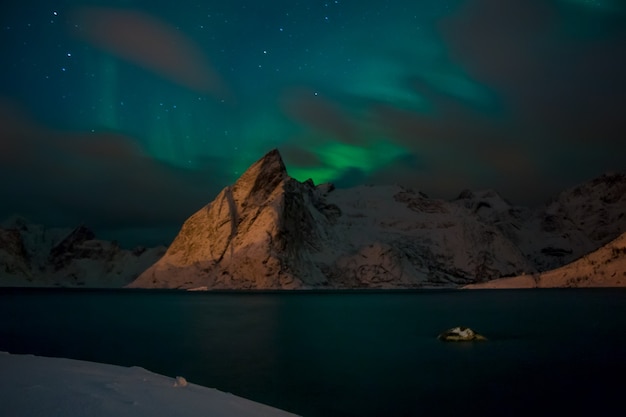 Noruega à noite. Fiorde de inverno rodeado por montanhas cobertas de neve. Luzes do norte e nuvens