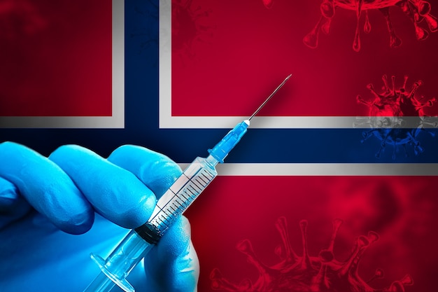 Noruega Campaña de vacunación Covid19 Mano en un guante de goma azul sostiene una jeringa delante de la bandera