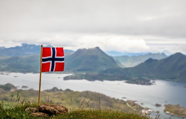 Norwegische Nationalflagge im Wind auf dem Gipfel des Nonstinden mit Fjord im Hintergrund Ballstad Vestvagoy Gemeinde Nordland County Norwegen