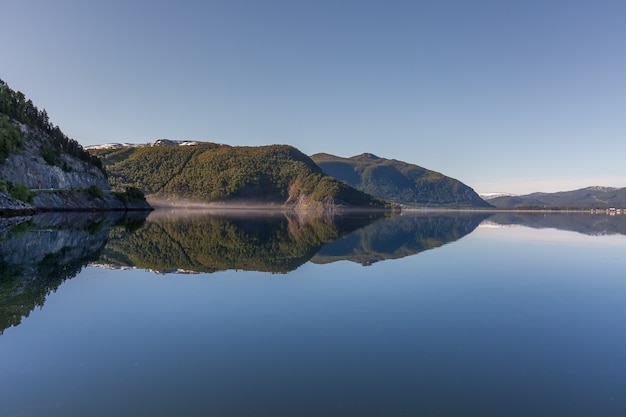 Norwegischer Fjord und Berge, umgeben von Wolken, Mitternachtssonne, Polartag, ideale Fjordreflexion in klarem Wasser