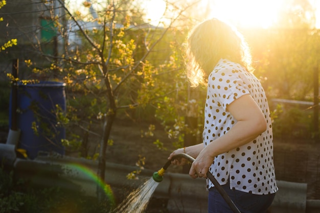 Nos raios de sol, uma mulher de cabelos encaracolados rega o jardim de uma mangueira com espaço de cópia de água