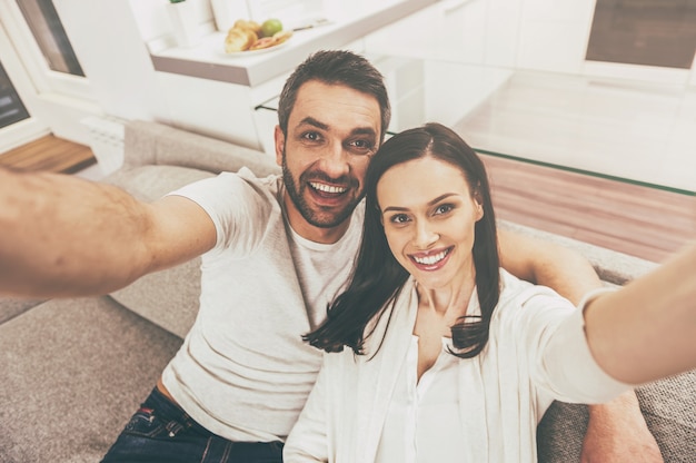 Nós somos bonitos! vista superior de um casal apaixonado e feliz se unindo e fazendo uma selfie enquanto estão sentados no sofá juntos