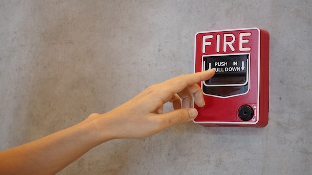 Not-Feueralarm oder Alarm- oder Klingelwarnausrüstung in roter Farbe mit Hand im Gebäude zur Sicherheit.