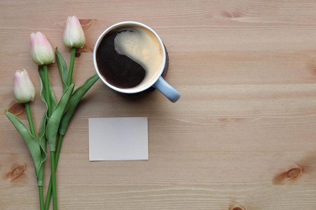 Nota adhesiva de la taza de café y tulipanes rosados en la mesa de madera