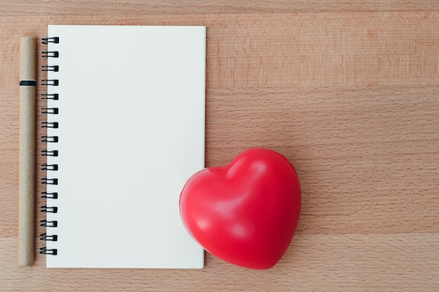 Foto nota en blanco con materiales de escritura y símbolo de corazón rojo en madera, utilizando como fondo