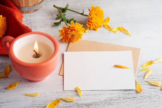 Nota en blanco y velas aromáticas encendidas de naranja y flores en la mesa rústica. Tarjeta de felicitación