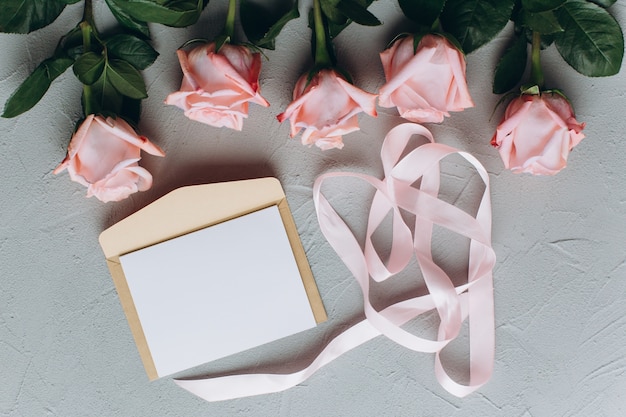 Nota de papel em branco com envelope, presentes e rosa-de-rosa