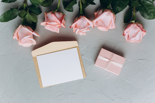 Nota de papel em branco com envelope, presentes e rosa-de-rosa