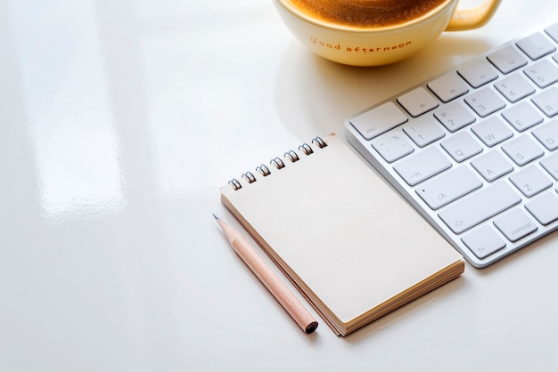 Nota em branco, lápis, teclado branco e café na mesa branca