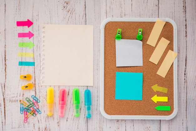 Notas adhesivas en tablero de corcho con papel de carta en blanco; resaltador y clips de papel sobre fondo de madera