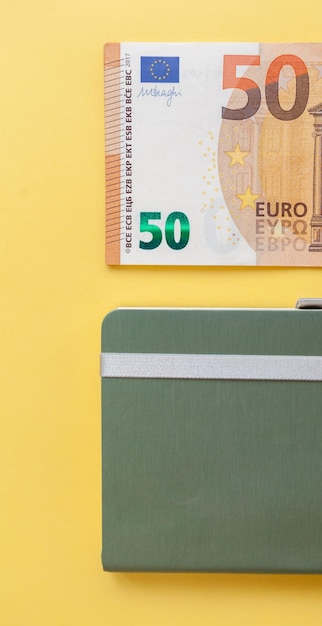 Notas de cinquenta euros dentro de uma carteira preta sobre fundo amarelo