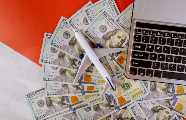 Notas de dólar americano com laptop e modelo de avião plástico