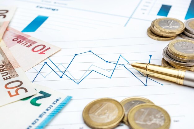 Notas e moedas de euro com caneta sobre o conceito de negócios de gráficos financeiros