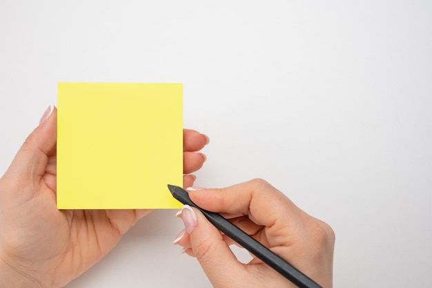 Notas escritas à mão lápis preto no fundo da mesa branca da etiqueta amarela maquete pegajosa folha de papel vazia para notas mão feminina segurando papel de nota e fazendo nota