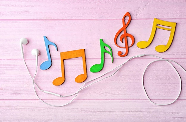 Notas musicales coloridas y auriculares sobre un fondo de madera rosa