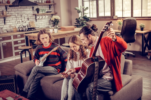 Notas sobre el teléfono. Tutor de guitarra de pelo oscuro barbudo enseñando a adolescente mostrando sus notas musicales en el teléfono