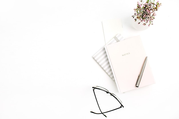 Notebook, Brille, Stift und Wildblumen auf weißem Hintergrund. Flache Lage, Ansicht von oben
