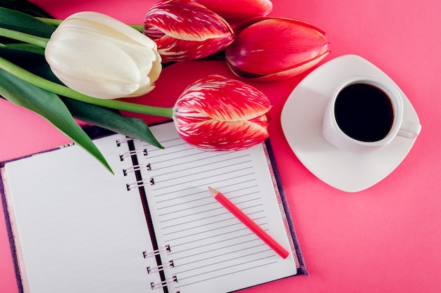 Notebook com uma xícara de café expresso e tulipas frescas em fundo rosa