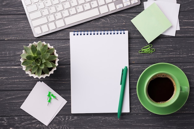 Notebook com xícara de café e planta suculenta na mesa de madeira