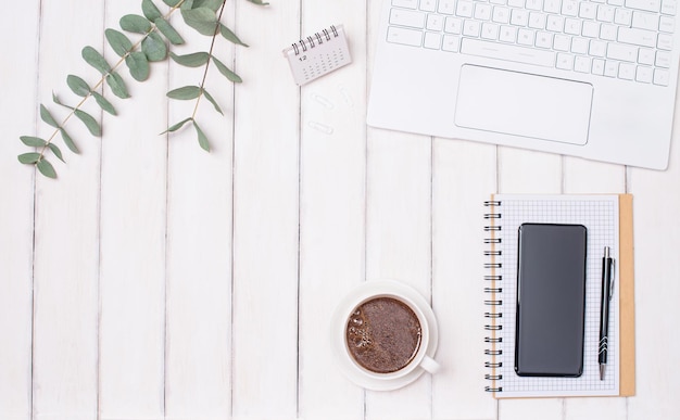 Notebook de smartphone de xícara de café portátil e galhos de eucalipto em fundo branco Conceito de espaço de trabalho feminino